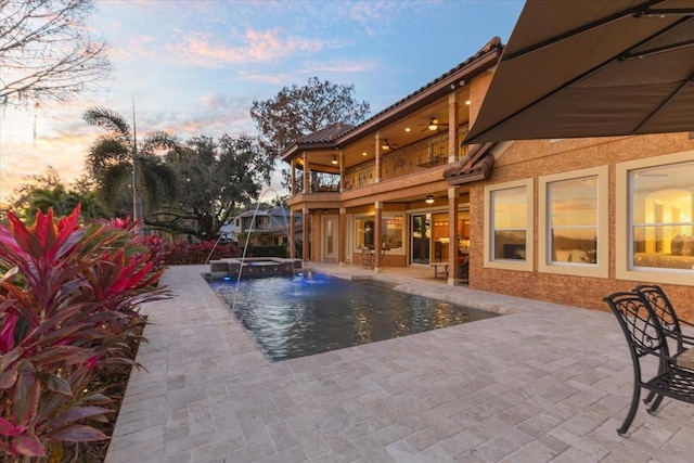 pool at dusk with pool water feature, an in ground hot tub, and a patio area