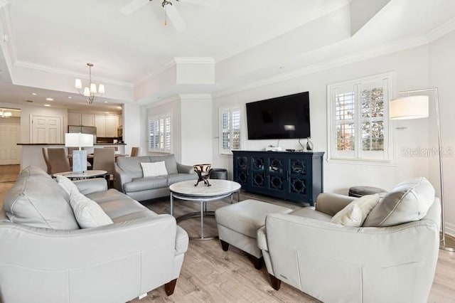 living room with ornamental molding, a healthy amount of sunlight, a tray ceiling, and light wood-type flooring