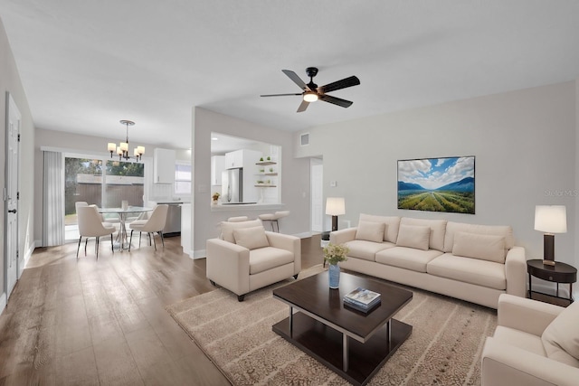 living room with ceiling fan with notable chandelier and light hardwood / wood-style flooring