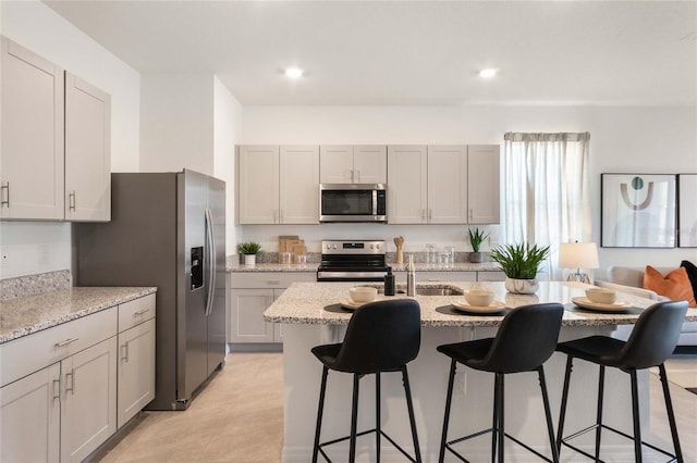 kitchen with sink, stainless steel appliances, a kitchen breakfast bar, light stone countertops, and a center island with sink