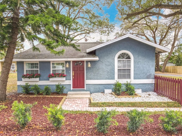 view of front of home with a shingled roof, fence, and stucco siding