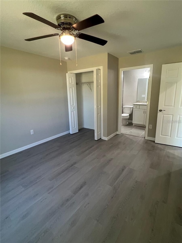 unfurnished bedroom featuring ensuite bath, wood-type flooring, a textured ceiling, a closet, and ceiling fan