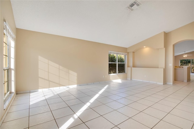 tiled empty room featuring vaulted ceiling and a textured ceiling