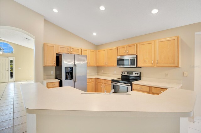 kitchen with lofted ceiling, light tile patterned flooring, stainless steel appliances, and light brown cabinets