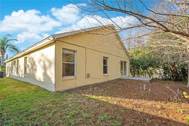 view of side of property featuring a yard, central AC, and a patio