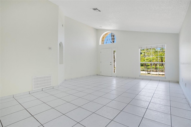 empty room featuring a textured ceiling, high vaulted ceiling, light tile patterned floors, and visible vents
