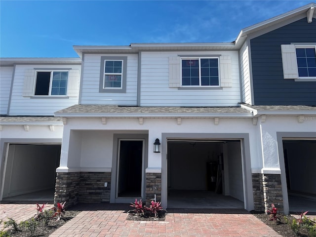 view of front of home with an attached garage, stone siding, decorative driveway, and roof with shingles