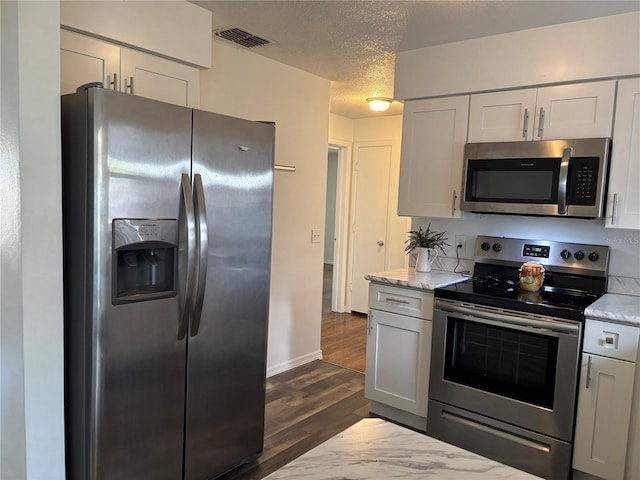 kitchen with white cabinetry, a textured ceiling, appliances with stainless steel finishes, dark hardwood / wood-style flooring, and light stone countertops