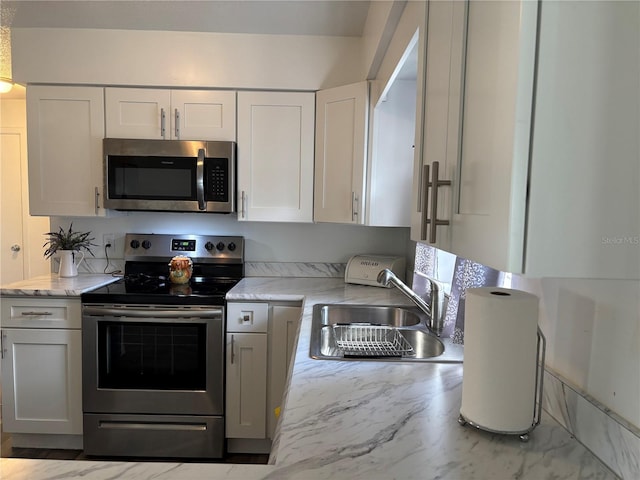 kitchen featuring stainless steel appliances, light stone countertops, sink, and white cabinets