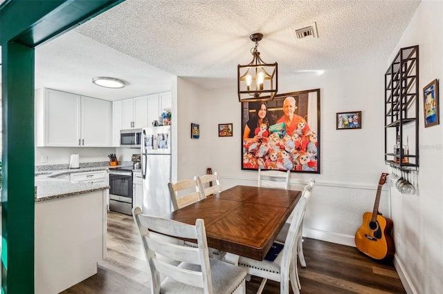 dining space with wood-type flooring, a chandelier, and a textured ceiling