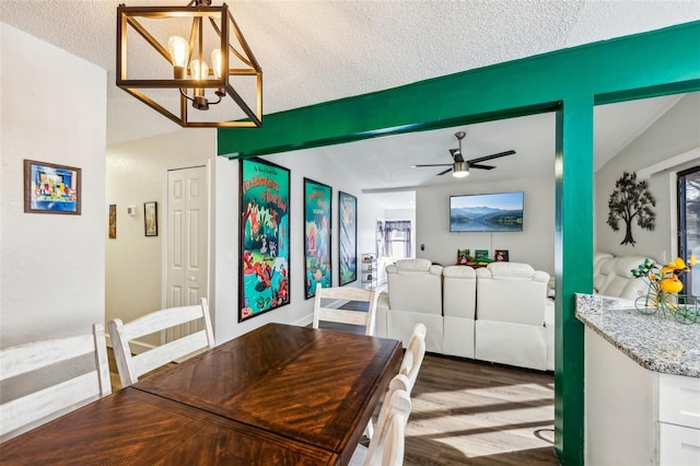 dining area featuring dark wood-type flooring, ceiling fan with notable chandelier, a textured ceiling, and beamed ceiling