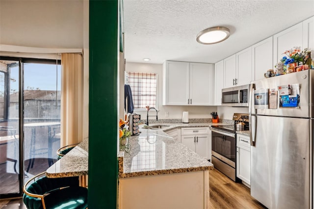 kitchen featuring white cabinetry, sink, light stone counters, stainless steel appliances, and light hardwood / wood-style flooring