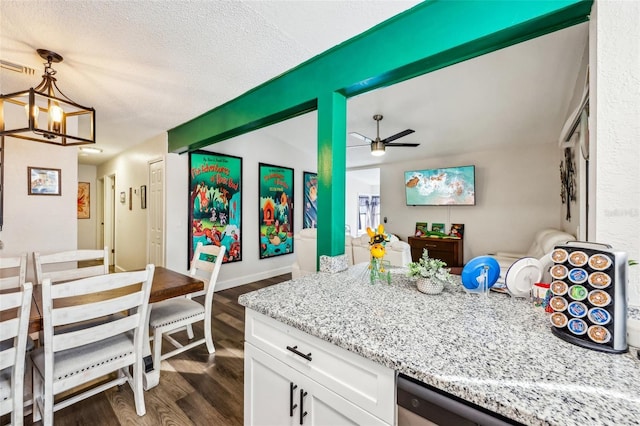 kitchen with dark wood-type flooring, a textured ceiling, light stone countertops, white cabinets, and decorative light fixtures