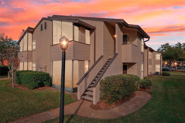 property exterior at dusk with stucco siding, a lawn, and stairs