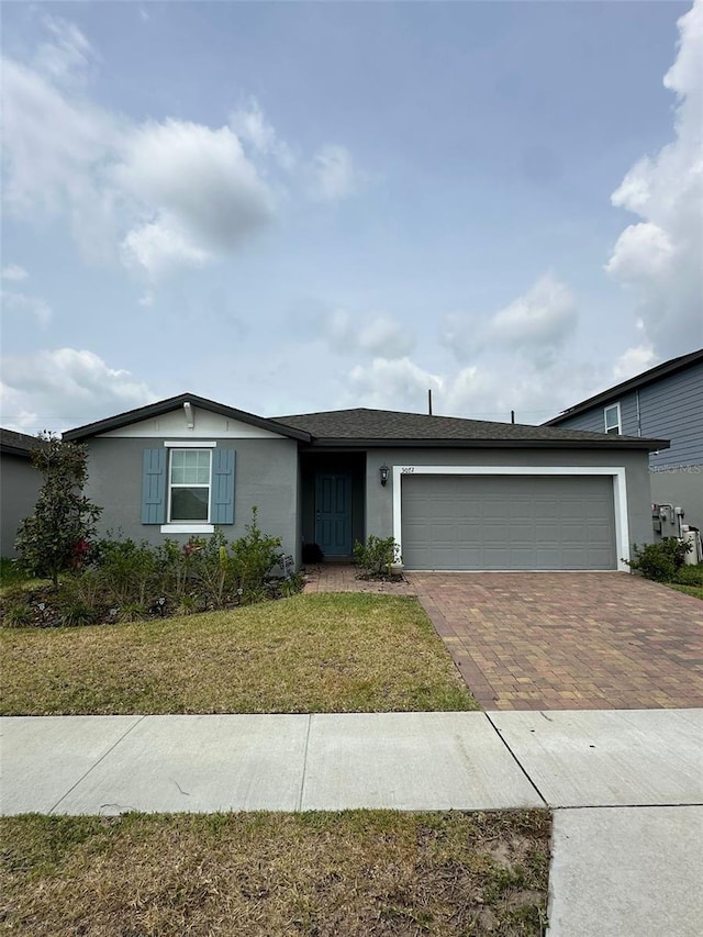 ranch-style house featuring a front lawn, decorative driveway, an attached garage, and stucco siding