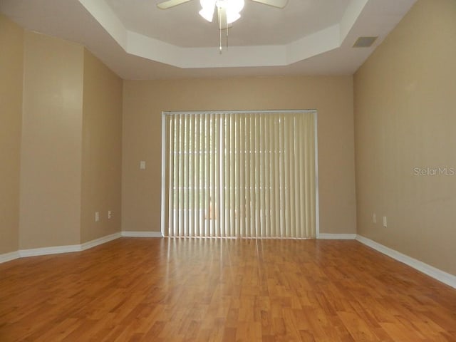 empty room with light hardwood / wood-style flooring, a raised ceiling, and ceiling fan