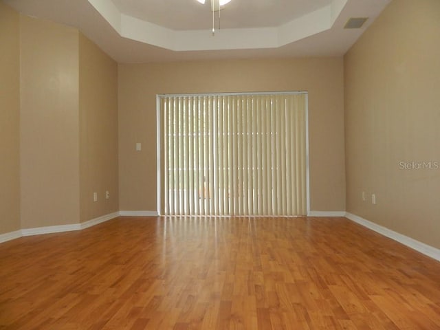 empty room featuring ceiling fan, a raised ceiling, and light wood-type flooring