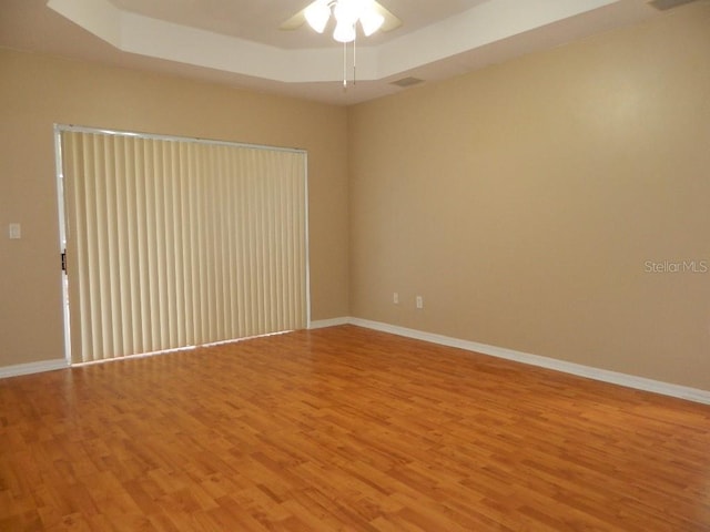 empty room featuring ceiling fan, light hardwood / wood-style floors, and a tray ceiling