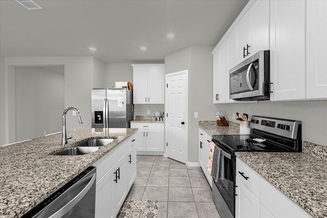 kitchen featuring appliances with stainless steel finishes, white cabinetry, sink, light tile patterned floors, and light stone countertops