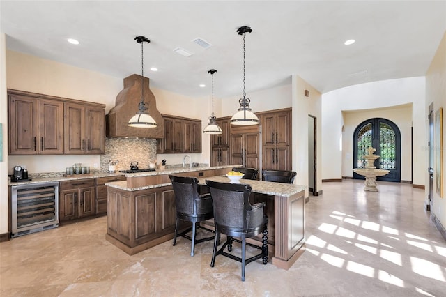 kitchen with wine cooler, decorative light fixtures, light stone countertops, and a center island with sink