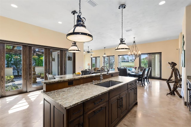 kitchen featuring pendant lighting, a kitchen island with sink, sink, and light stone counters