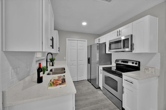 kitchen featuring white cabinetry, sink, backsplash, light hardwood / wood-style floors, and stainless steel appliances