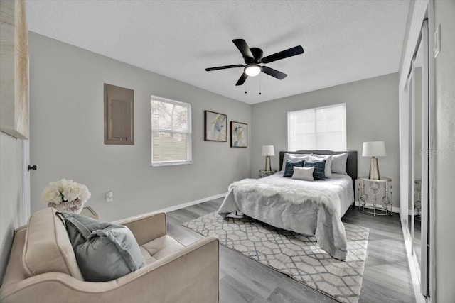 bedroom with ceiling fan, wood-type flooring, electric panel, and a textured ceiling