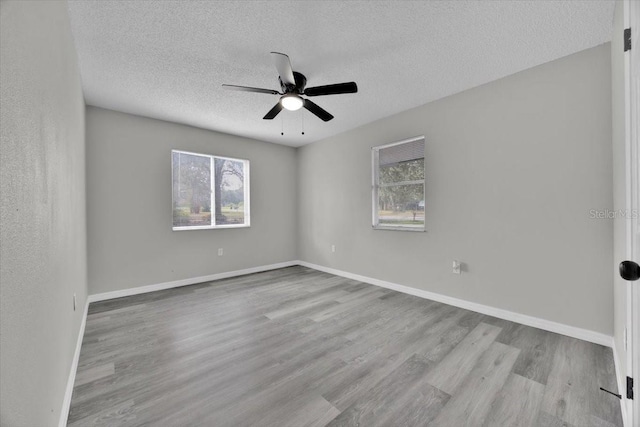 unfurnished room with ceiling fan, a wealth of natural light, a textured ceiling, and light hardwood / wood-style floors