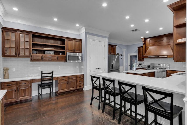 kitchen with crown molding, a breakfast bar, appliances with stainless steel finishes, built in desk, and ornate columns