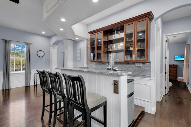 bar featuring light stone counters, decorative backsplash, dark hardwood / wood-style floors, and ornate columns