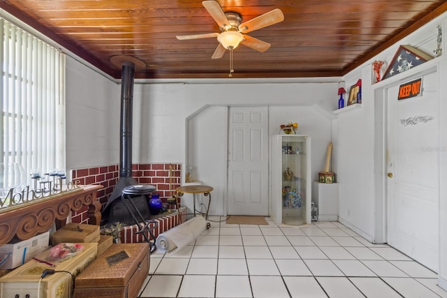 interior space with light tile patterned flooring, a wood stove, ceiling fan, and wood ceiling