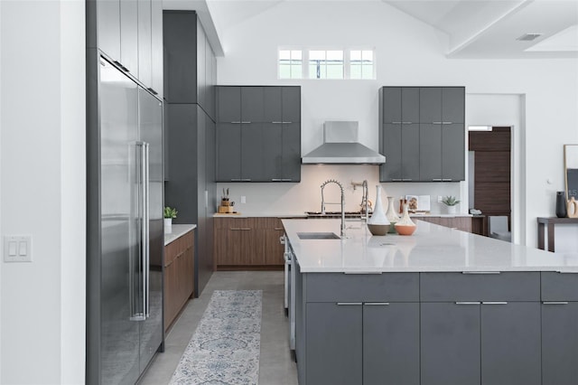 kitchen with built in fridge, wall chimney range hood, gray cabinetry, and light stone counters