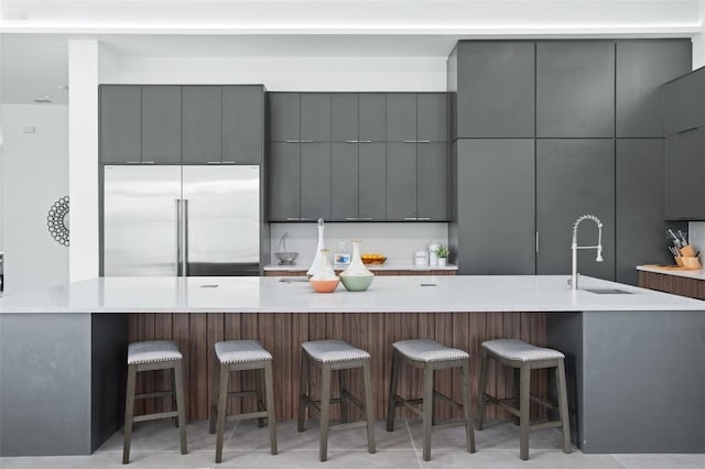 kitchen with built in refrigerator, sink, gray cabinetry, and a kitchen bar