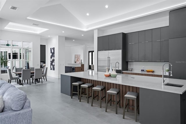 kitchen featuring a large island with sink, stainless steel built in refrigerator, sink, and a kitchen breakfast bar