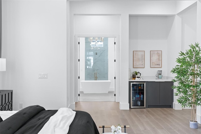 bedroom featuring wine cooler, connected bathroom, bar area, and light hardwood / wood-style flooring