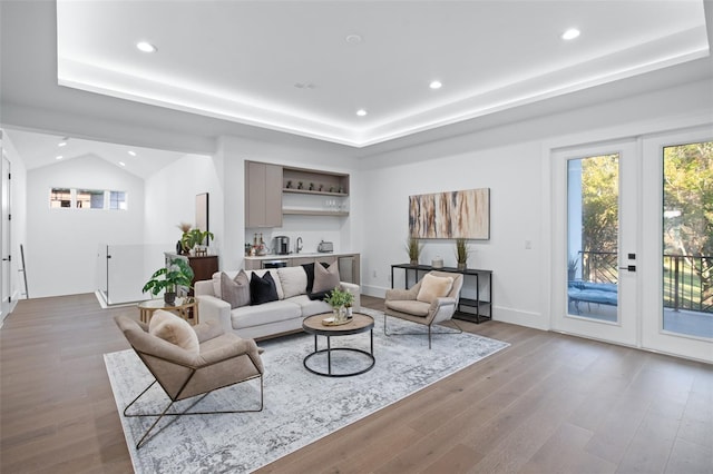 living room featuring vaulted ceiling, bar, a tray ceiling, and light hardwood / wood-style floors