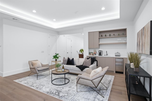 living room with a tray ceiling, wet bar, and wood-type flooring