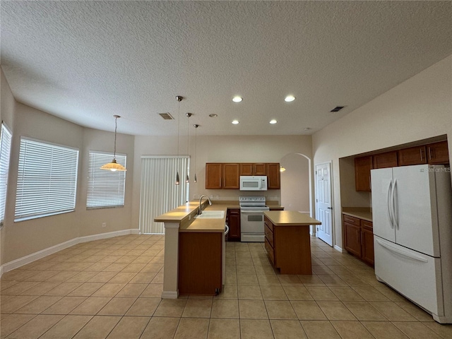 kitchen featuring sink, decorative light fixtures, light tile patterned floors, an island with sink, and white appliances