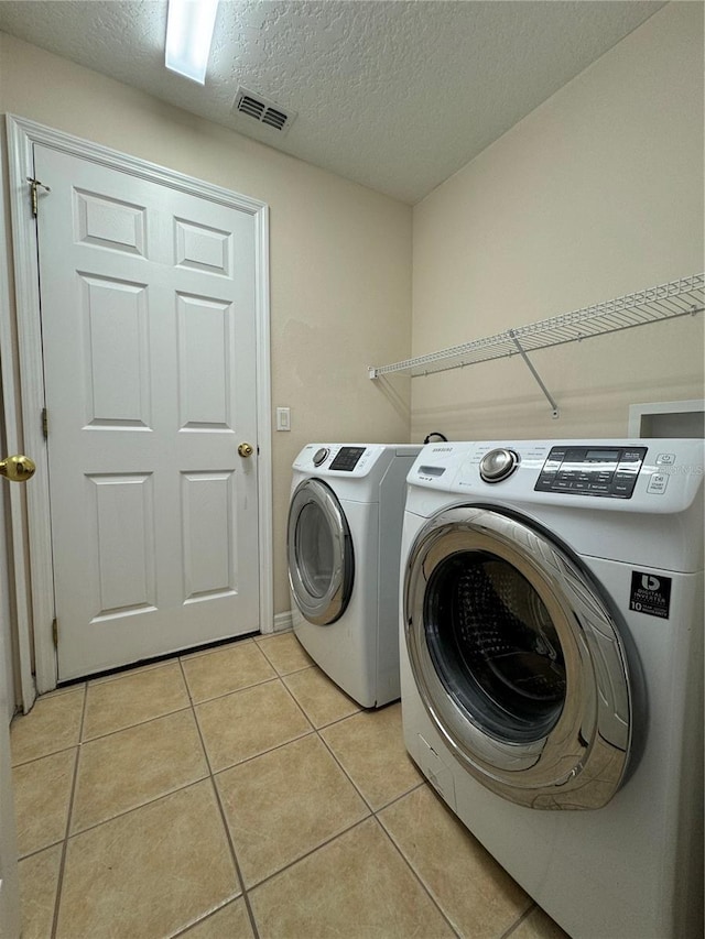 laundry room with light tile patterned flooring, washer and dryer, and a textured ceiling