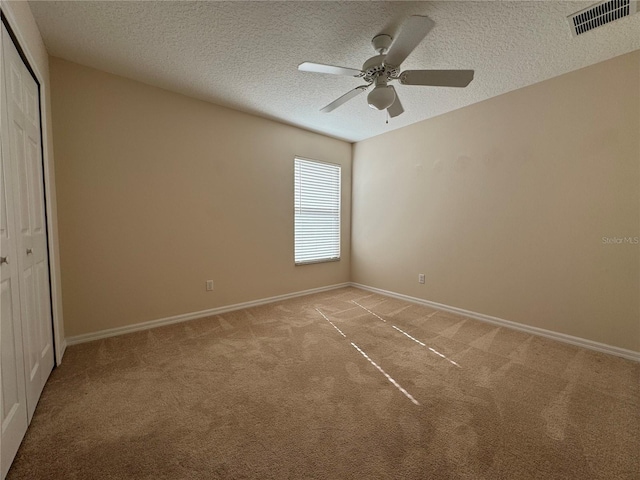 unfurnished bedroom with light carpet, ceiling fan, a closet, and a textured ceiling