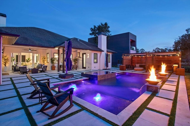 pool at dusk with pool water feature, a patio area, an in ground hot tub, ceiling fan, and an outdoor living space with a fire pit