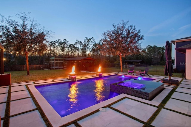 pool at dusk featuring pool water feature, a patio area, an outdoor fire pit, a yard, and an in ground hot tub