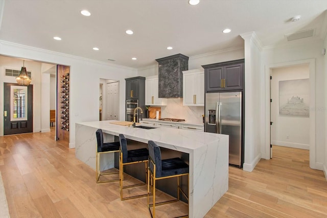 kitchen featuring a breakfast bar, sink, a large island with sink, light stone counters, and stainless steel appliances