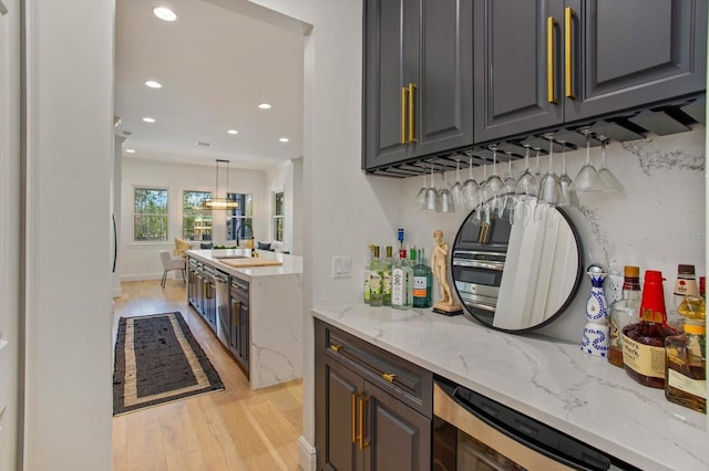 bar featuring decorative light fixtures, sink, wine cooler, light stone counters, and light hardwood / wood-style floors