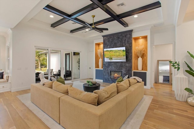 living room featuring coffered ceiling, light wood-type flooring, a tile fireplace, a towering ceiling, and beam ceiling