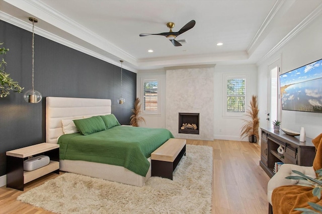 bedroom with ornamental molding, a tray ceiling, multiple windows, and light hardwood / wood-style flooring