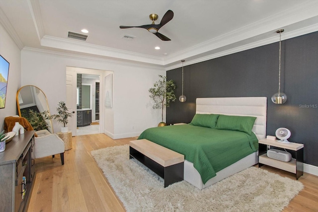 bedroom featuring ceiling fan, connected bathroom, a tray ceiling, wood-type flooring, and ornamental molding