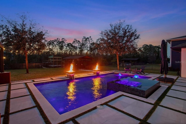 pool at dusk with a fire pit, a lawn, a patio, and an in ground hot tub