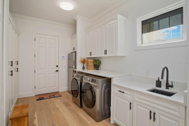 washroom featuring sink, crown molding, light hardwood / wood-style flooring, cabinets, and separate washer and dryer