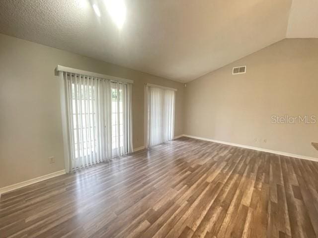 empty room featuring dark wood-type flooring, a textured ceiling, and vaulted ceiling